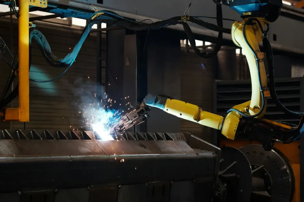 Yellow robotic arm spot welding a piece of steel